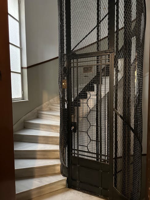 A multi-story staircase viewed from above, showing a series of square landings and metal railings painted black, inside a building with white walls. The staircase is enclosed within the interior space, and a central light fixture at the top provides illumination. The image captures the vertical layout and construction of the staircase, illustrating potential challenges in moving furniture or packing boxes between floors during a home relocation or removal service. Man and a Van Marylebone specializes in furniture transport and packing for house removals, often managing access issues like staircase and lift difficulties, as seen in this environment. The photo highlights the internal environment where careful planning is necessary to navigate narrow or complex staircases during the loading process, emphasizing the importance of professional removals services for efficient and safe relocation solutions.